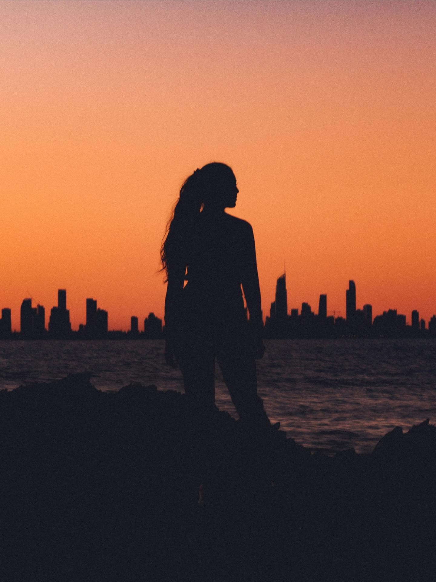 Frau steht vor einer Skyline während des Sonnenuntergangs