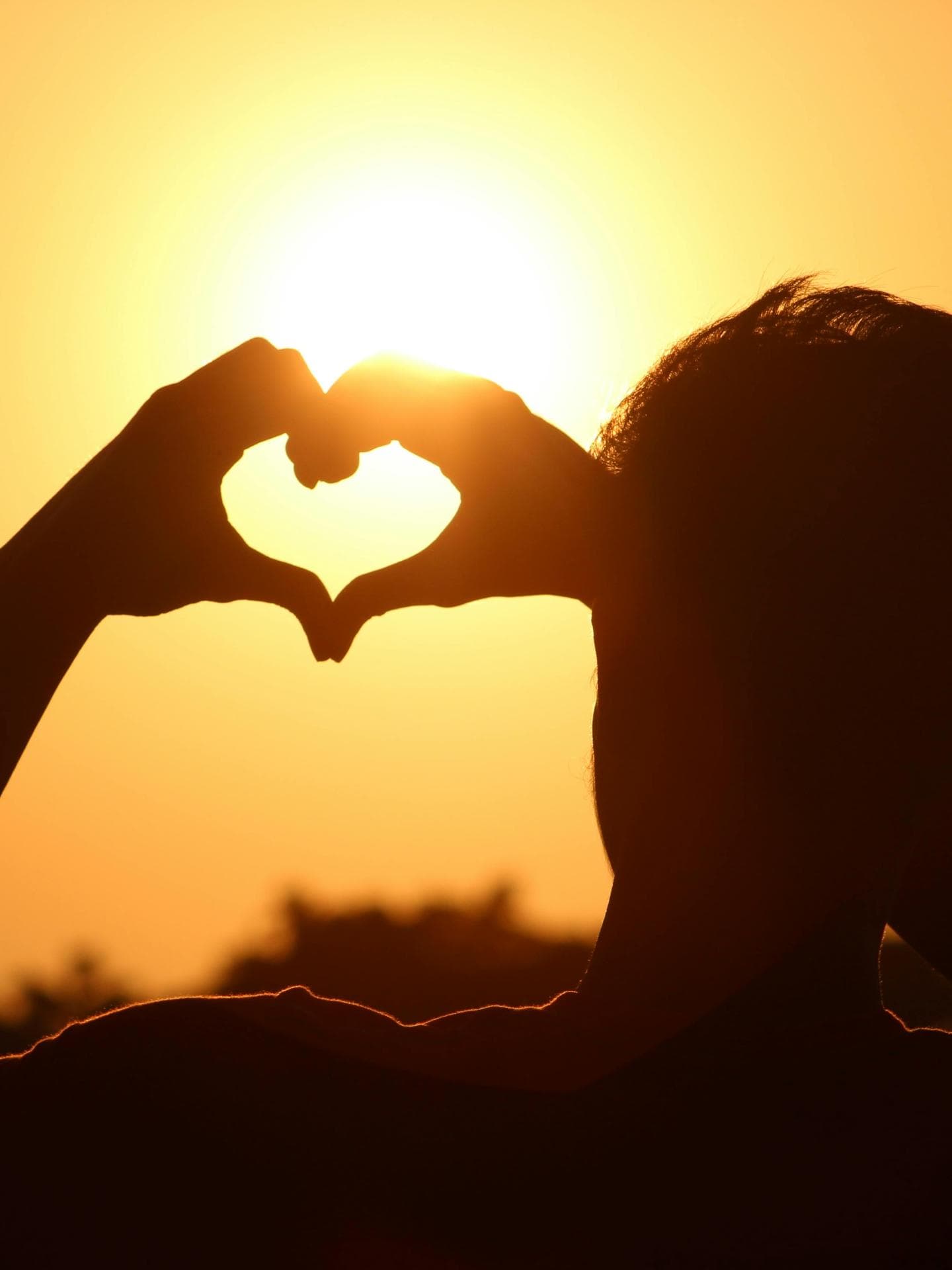 Person zeigt Herz vor Sonne