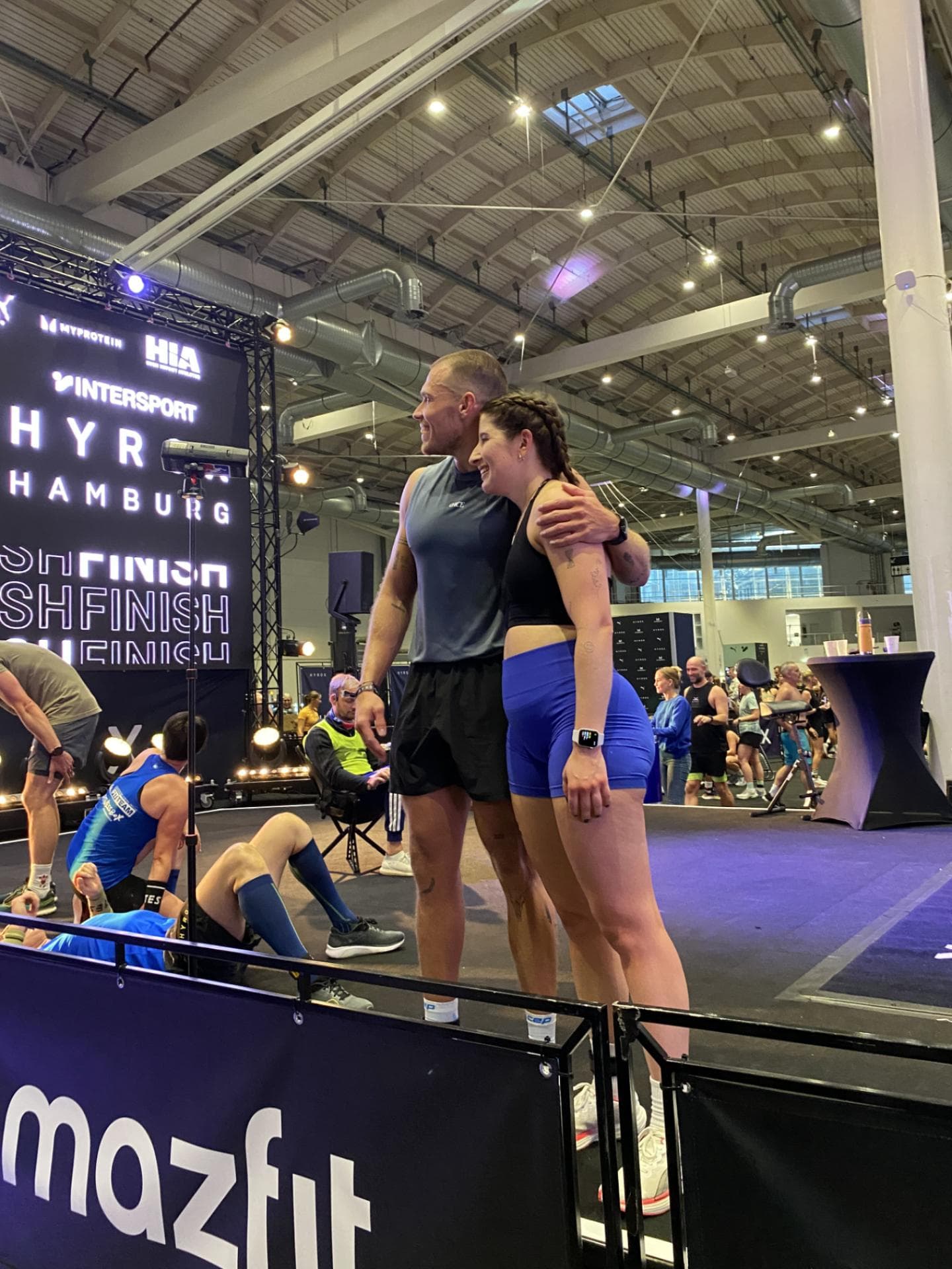 Nach dem Hyrox-Race war die Freude bei Redakteurin Laura und ihrem Freund riesig. Eine Frau und ein Mann in Sportkleidung gucken Arm in Arm nach links.