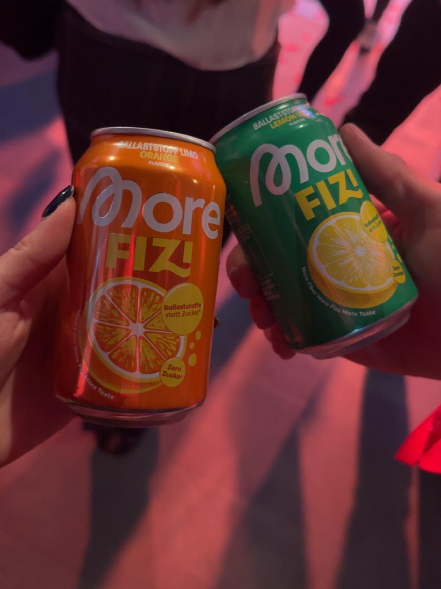 More Fizi Dosen in Orange und Grün in der Hand.