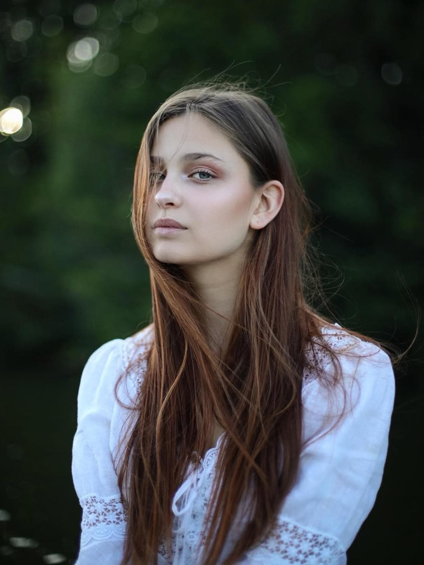 Anastasia hatte vor GNTM lange braune Haare. Eine junge Frau mit langen braunen Haaren und einer weißen Bluse mit Spitzeneinsätzen.