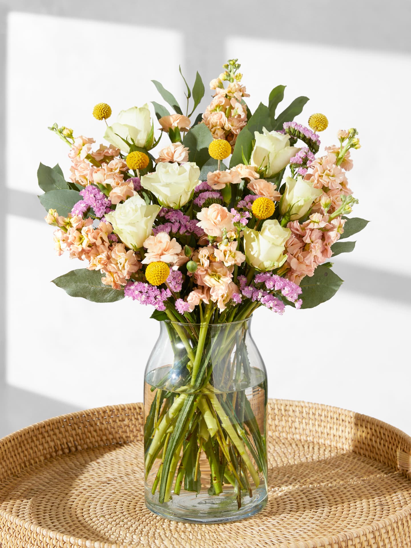 Bloom & Wild Blumenstrauß in einer Vase auf einem Rattantablett.