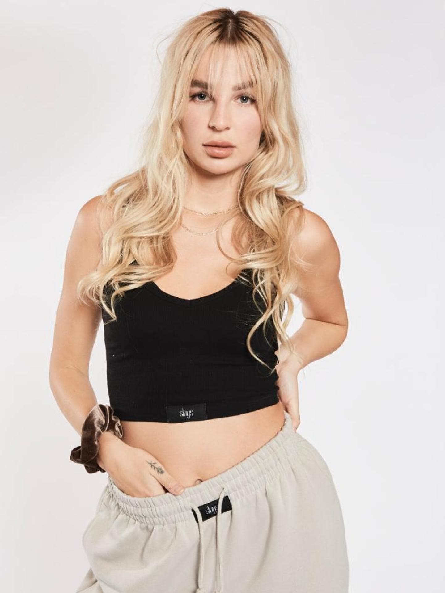 Mareike von GNTM hatte früher lange blonde Haare. Eine junge Frau mit blonden langen Haaren, einem schwarzen Top und einer grauen Jogginghose.