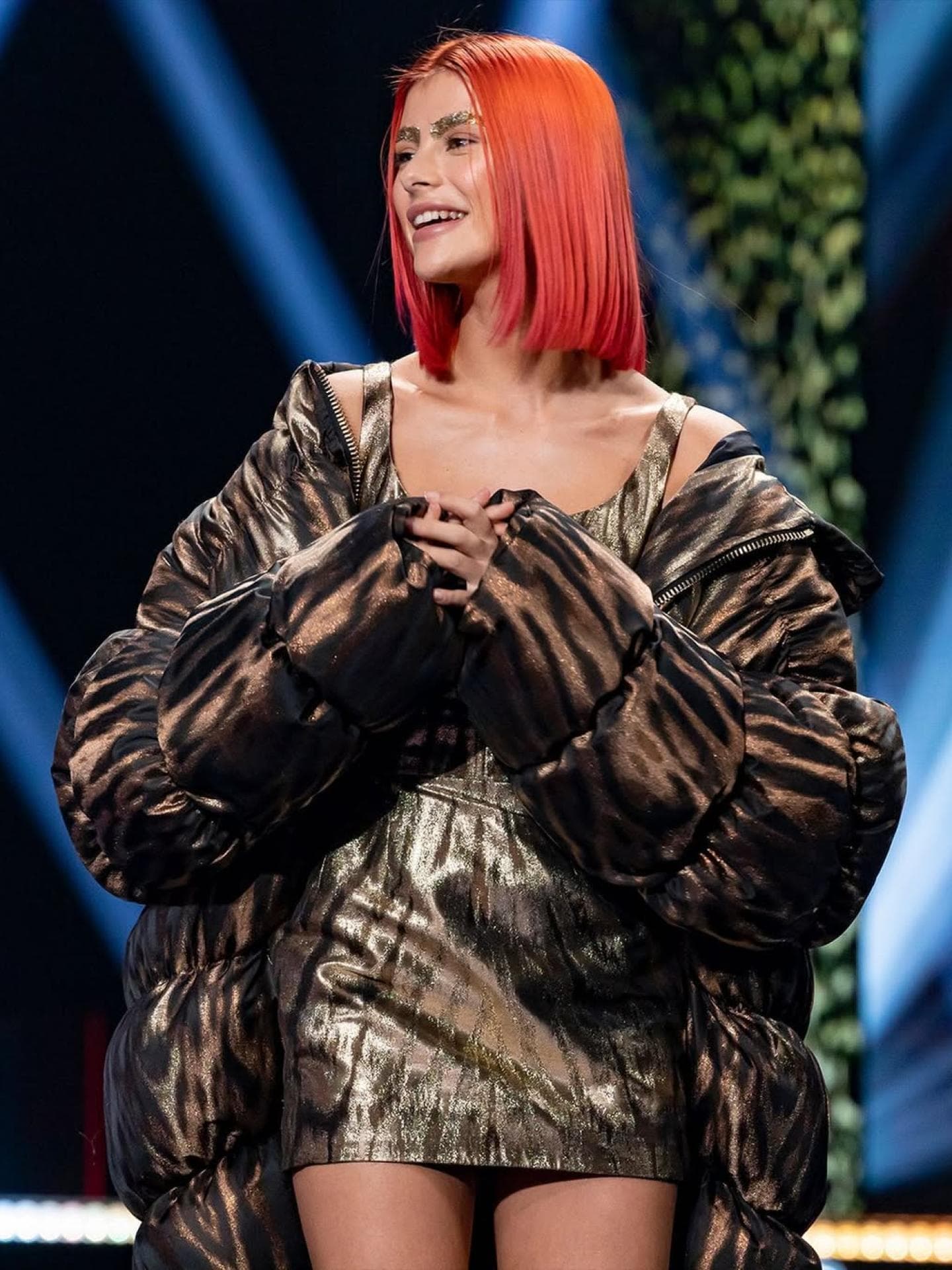 Romina Palm bekam bei GNTM rote Haare. Eine junge Frau mit kurzen, roten Haaren und einem schimmernden Outfit.