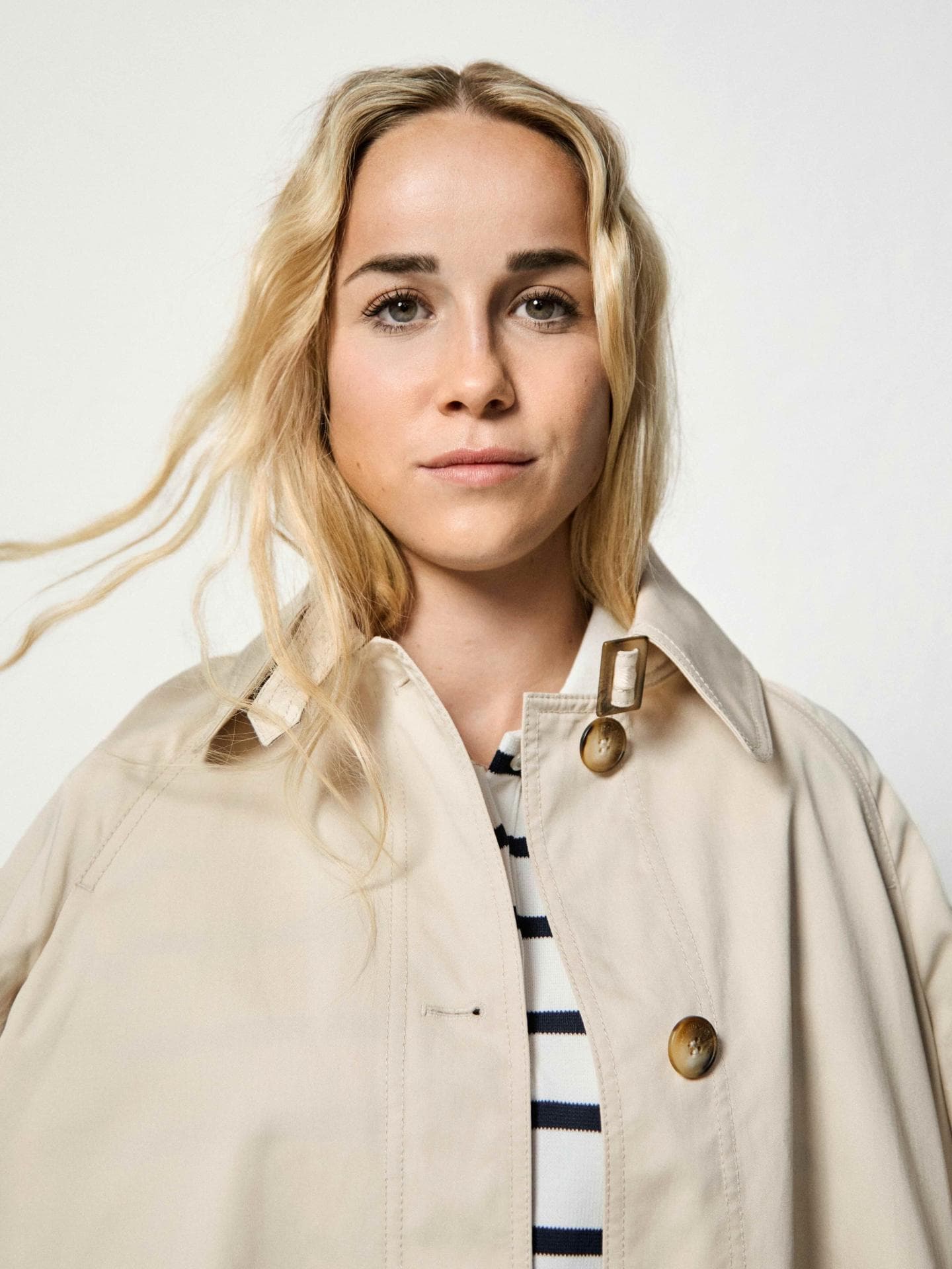 Der „casual-elegant“-Look von TK Maxx ist genau Giulias Stil: Ausgestellter Trenchcoat, Marinière im Polo-Stil, High-Waist-Jeans, Pantoletten, Ohrringe und Ringe von TK Maxx.