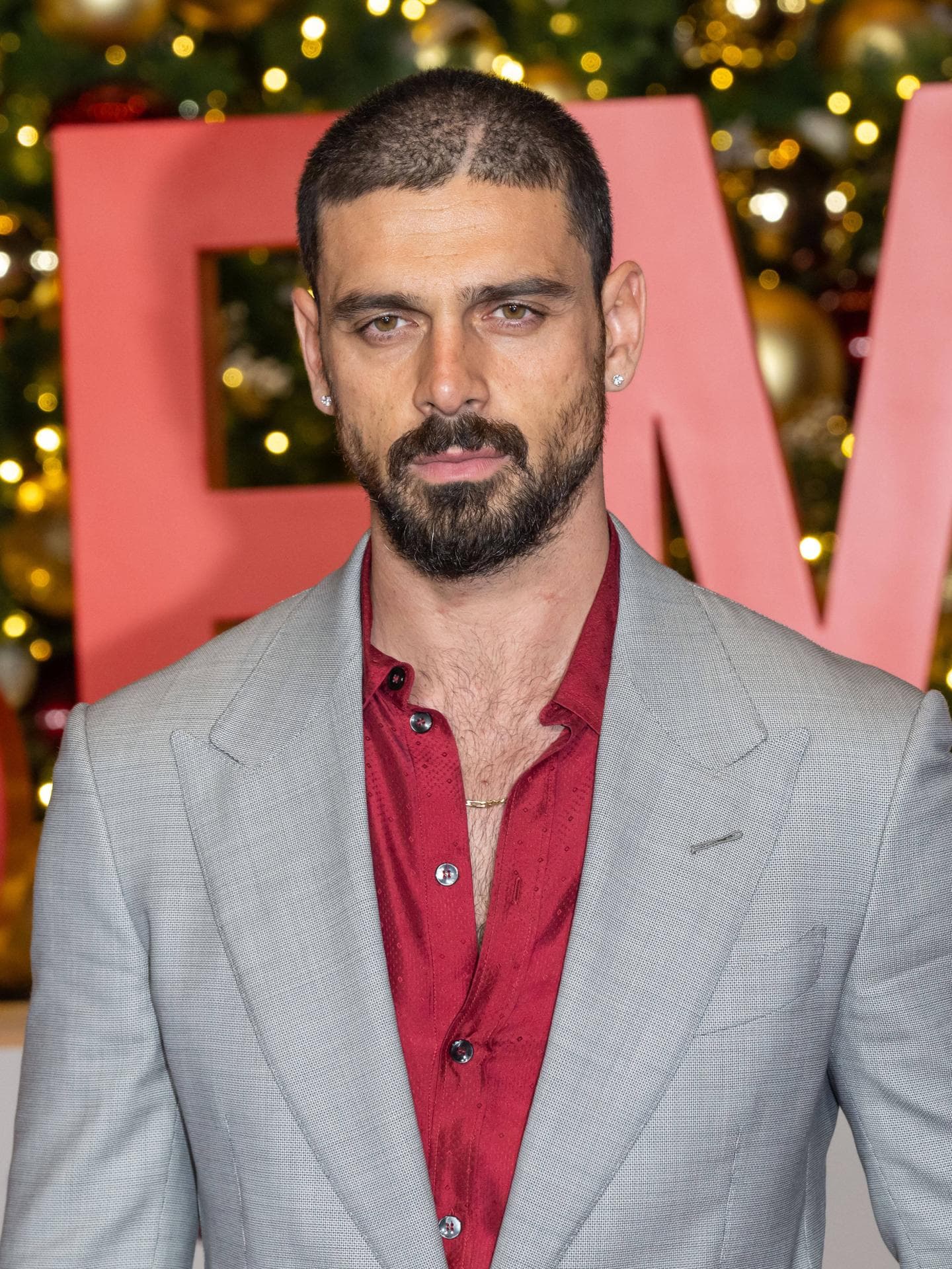 Michele Morrone spielte bei „The Housemaid“ mit. Michele Morrone in einem grauen Anzug mit rotem Hemd darunter.