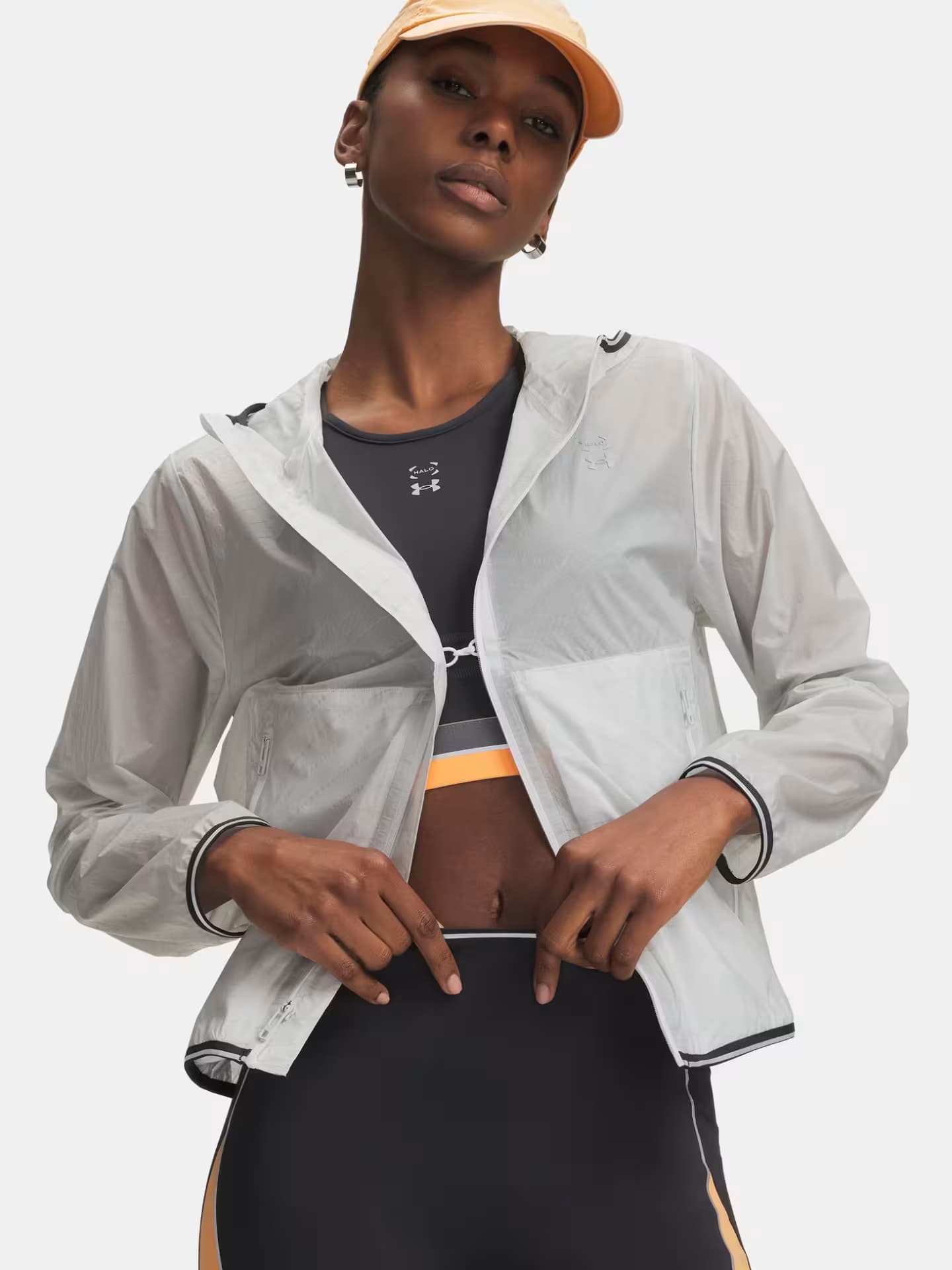Dunkelhäutige Frau trägt Sportkleidung und eine Kappe sowie eine transparente Laufjacke.