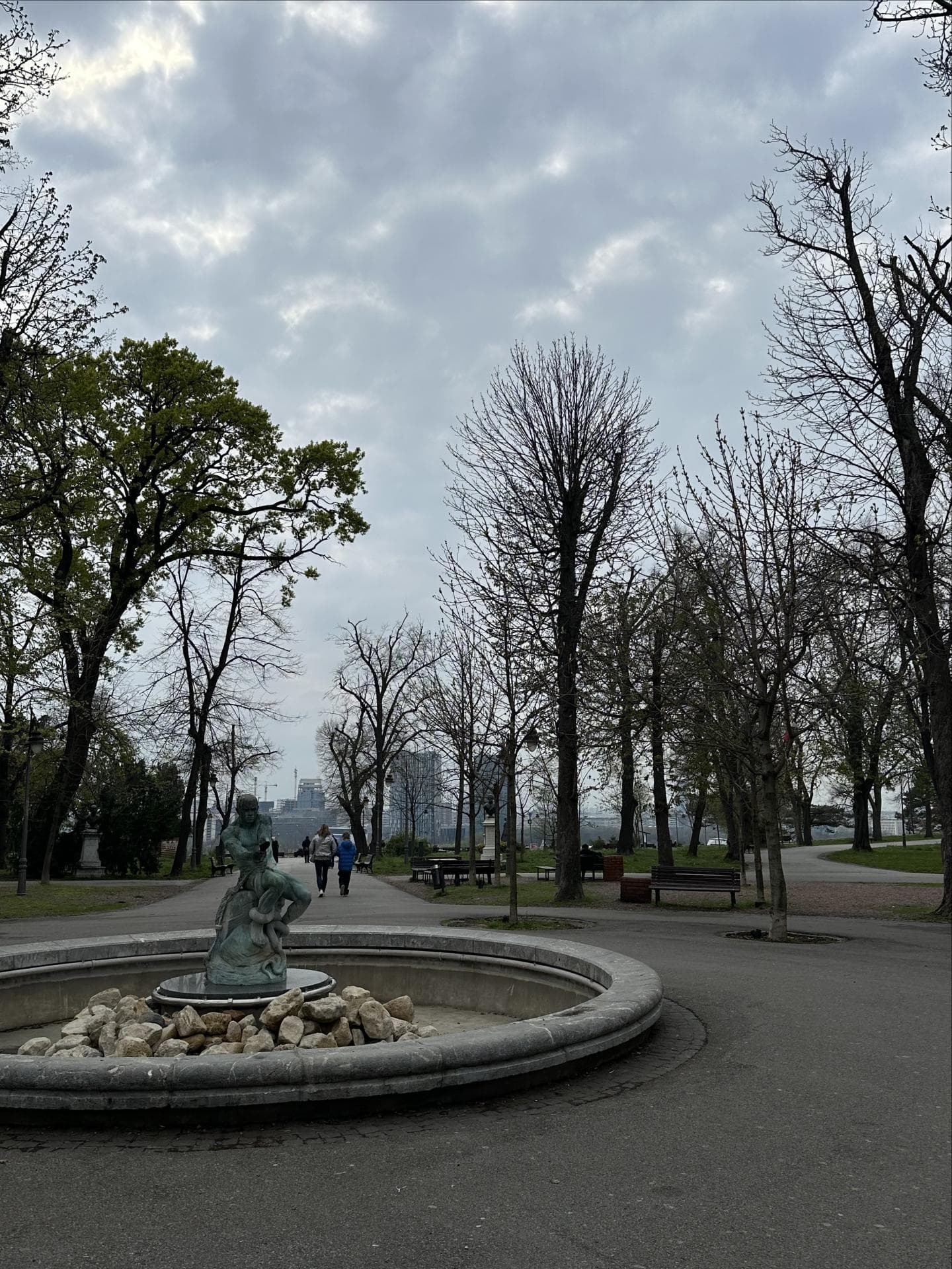 Ein Park in Belgrad mit einem Springbrunnen ohne Wasser und Bäumen im Hintergrund.