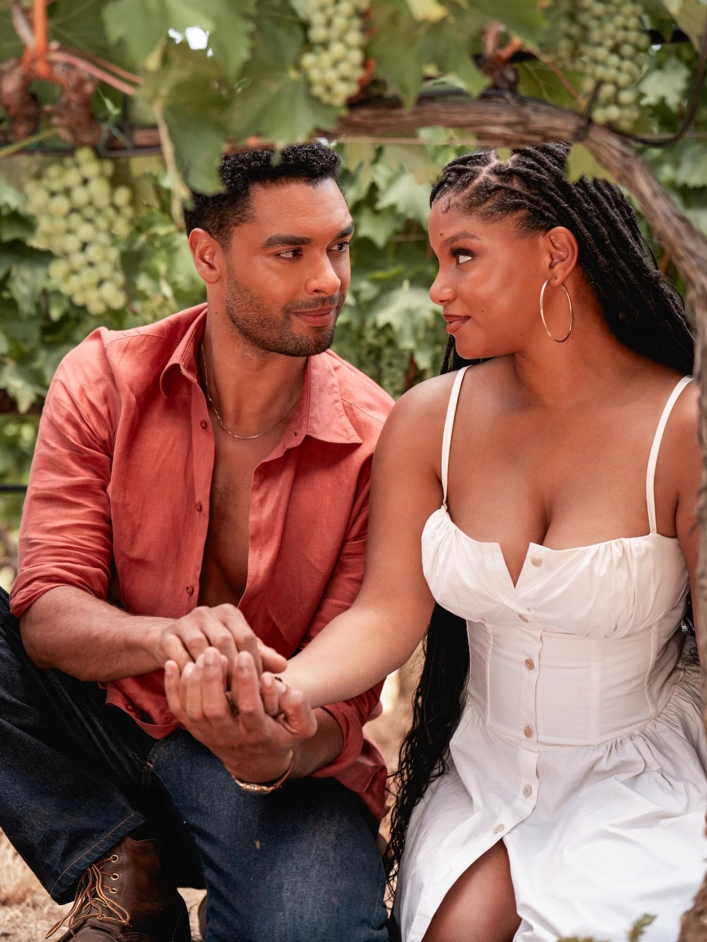Mit Halle Bailey als Anna und Regé-Jean Page als Michael haben die Regisseure die perfekte Besetzung für die Story gefunden. Ein junger Mann in einem rötlichen Hemd und eine junge Frau in einem weißen Kleid sitzen händchenhaltend nebeneinander und schauen sich tief in die Augen.