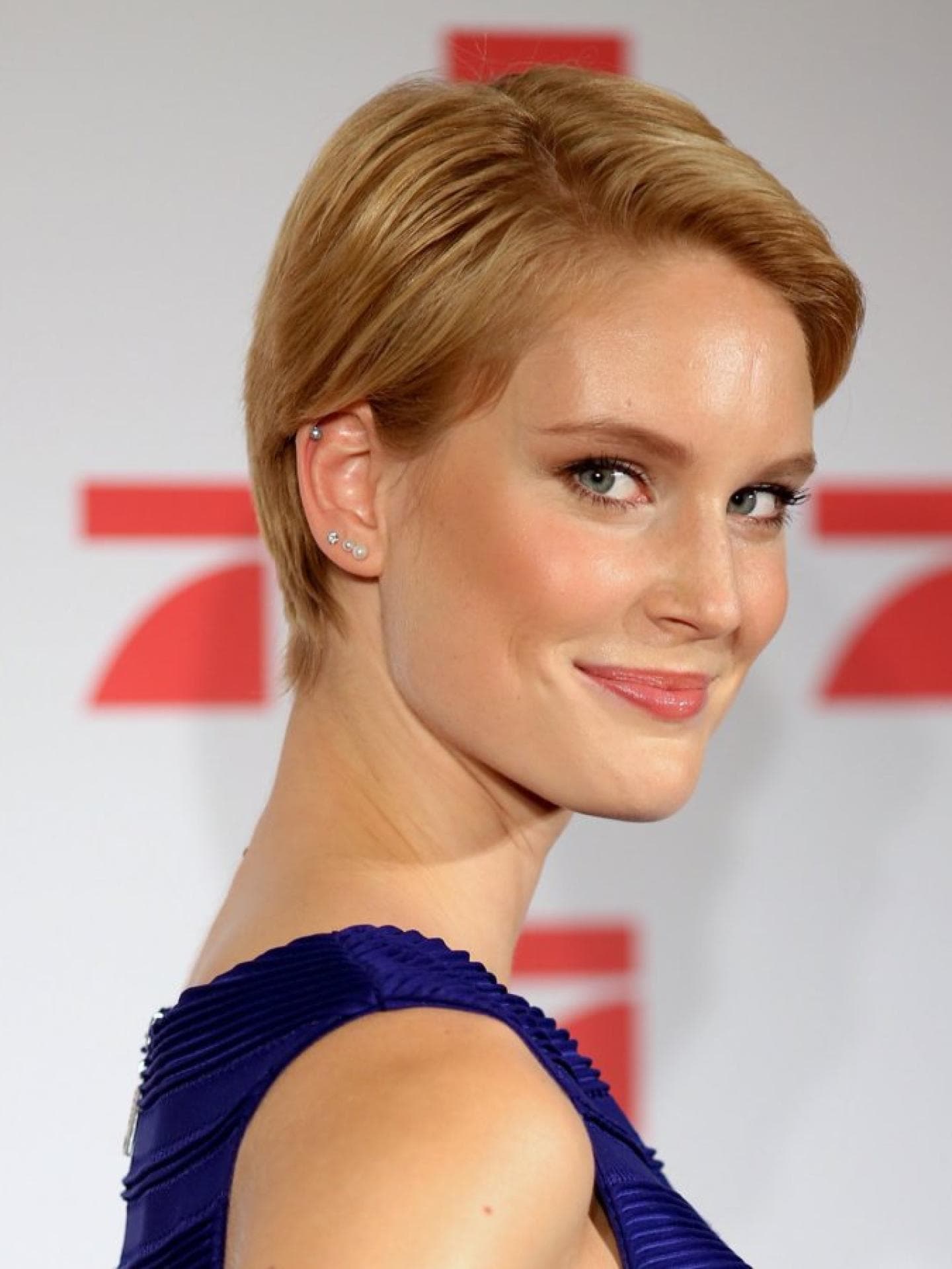 Nach GNTM hatte Kim Hnizdo kurze Haare. Kim Hnizdo mit kurzen Haaren und einem blauen Oberteil guckt über die Schulter in die Kamera.