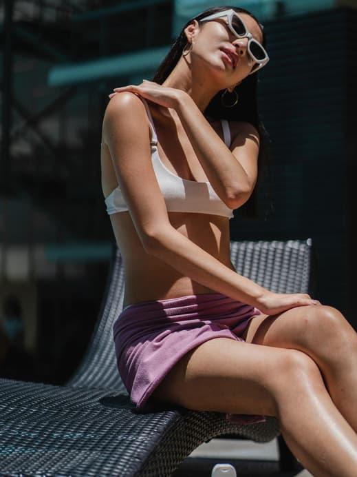 Eine Frau mit Bikinioberteil und Sonnenbrille trägt Sonnenschutz am Hals auf.