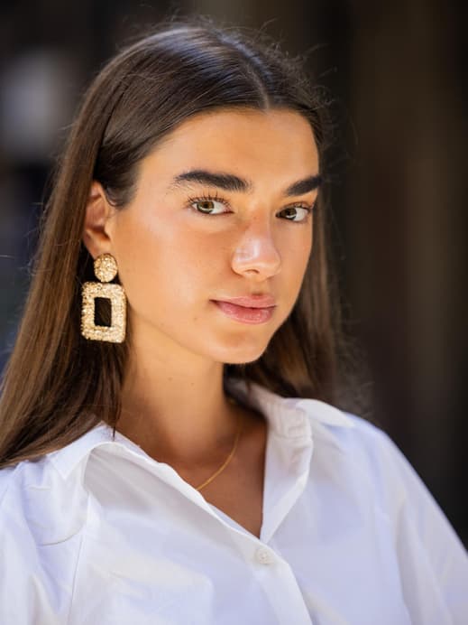 Frau mit Sommerteint und braunen offenen Haaren sowie großen Ohrringen.