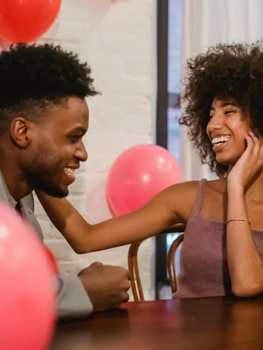Mann und Frau sitzen am Tisch mit Luftballons und lachen
