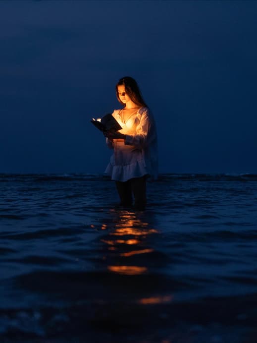 Frau steht im Meer und liest ein Buch