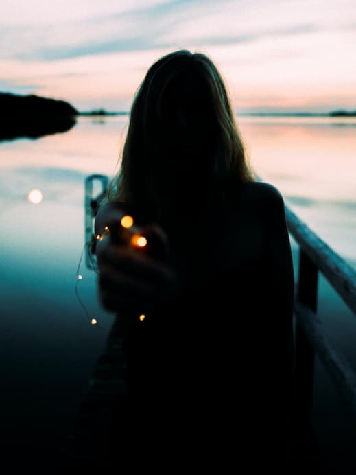 Frau steht am See mit einer Lichterkette