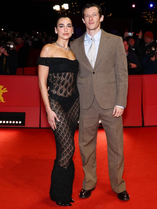 Dua Lipa in einem schwarzen Spitzenkleid und Callum Turner in einem braunen Anzug.