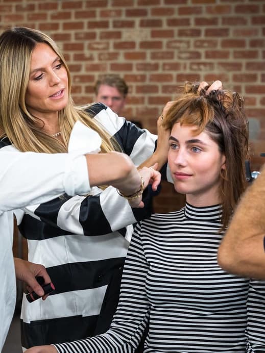 Am Set von Germany's Next Topmodel beim Umstyling steht Heidi Klum mit einer Friseurin bei einer Kandidatin.