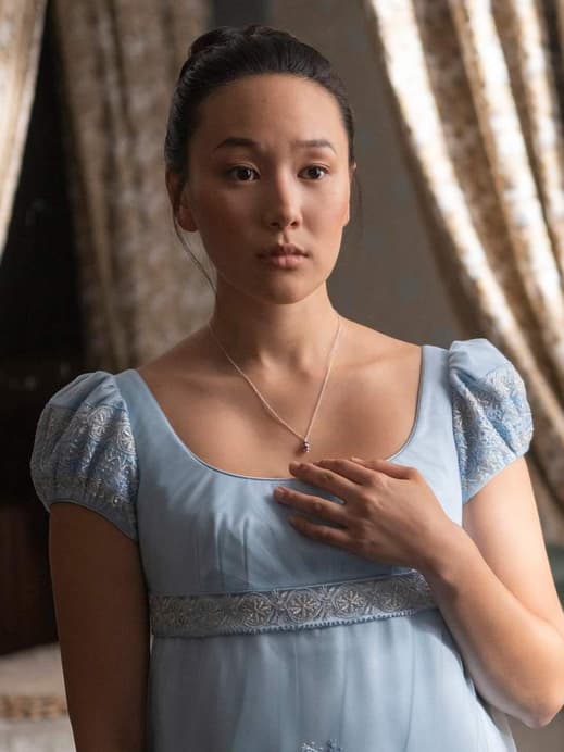 Eine junge Frau in einem babyblauen Kleid guckt starr nach vorn und fasst sich an ihr Dekollete.