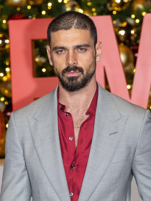 Michele Morrone in einem grauen Anzug mit rotem Hemd darunter.