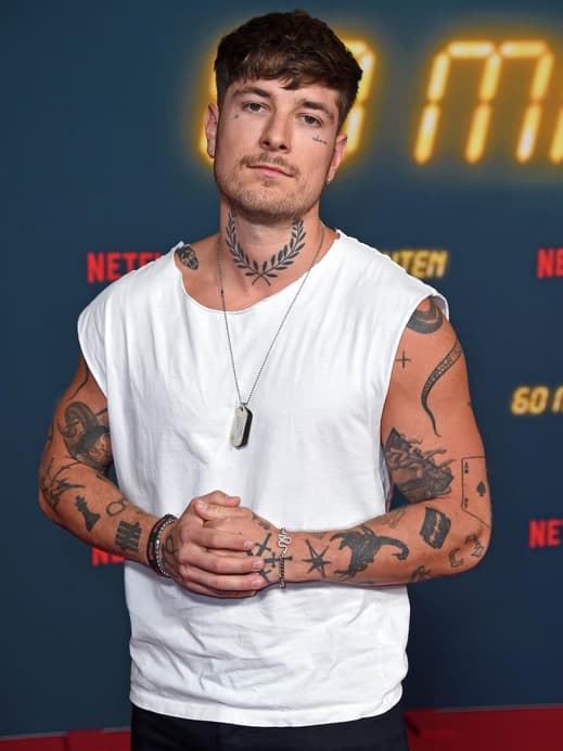 Willi Banner mit einem weißen Tanktop, einer Kette und voll tattoowierten Armen.