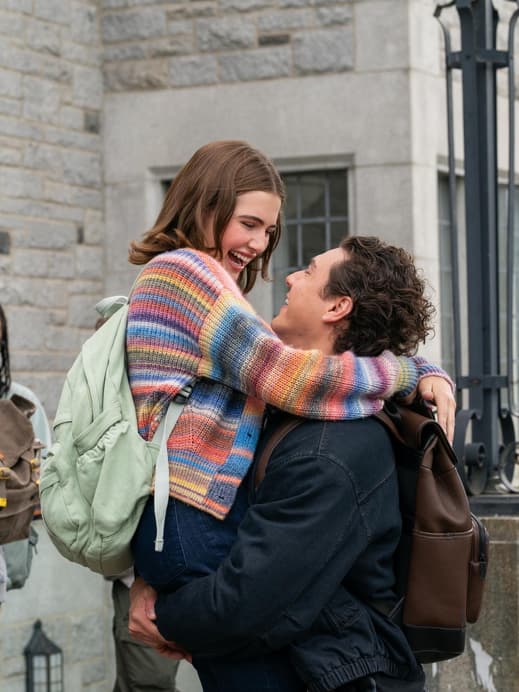 Eine junge Frau mit einem bunt gestreiften Cardigan wird von einem Mann hochgehoben.