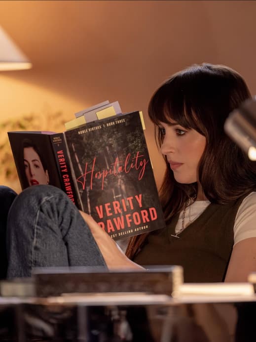 Dakotha Johnson sitzt in einem Zimmer mit gedämmtem Licht und liest ein Buch.