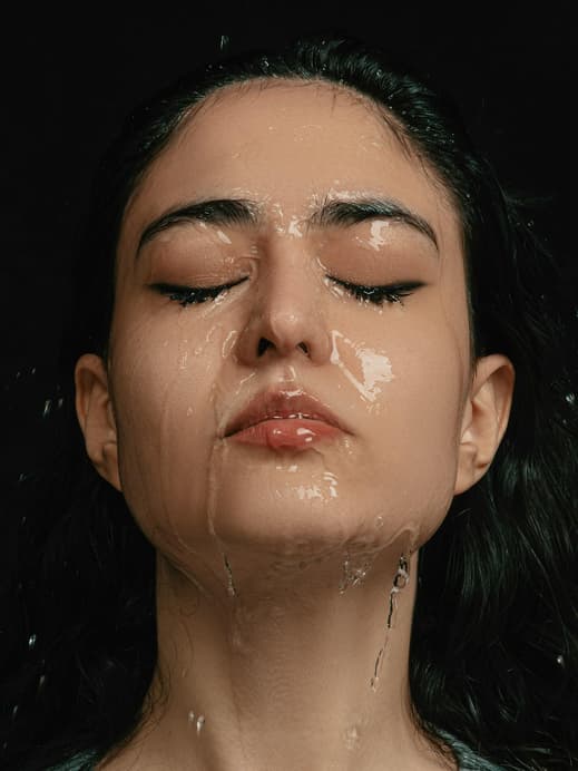 Einer Frau mit geschlossenen Augen läuft Wasser über das komplette Gesicht.