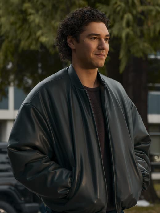 Ein junger Mann mit dunklen Locken in einer Lederjacke steht mit seinen Händen in der Tasche und guckt zur Seite.