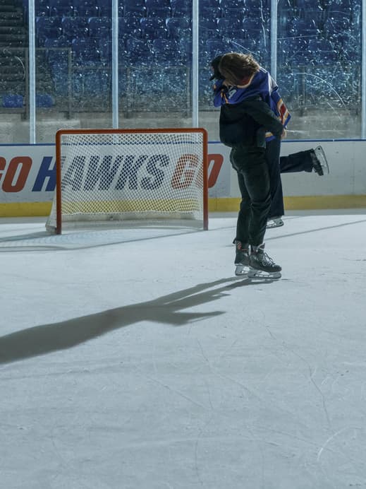 Ein Mann und eine Frau fallen sich auf einem Eishockeyfeld in die Arme.