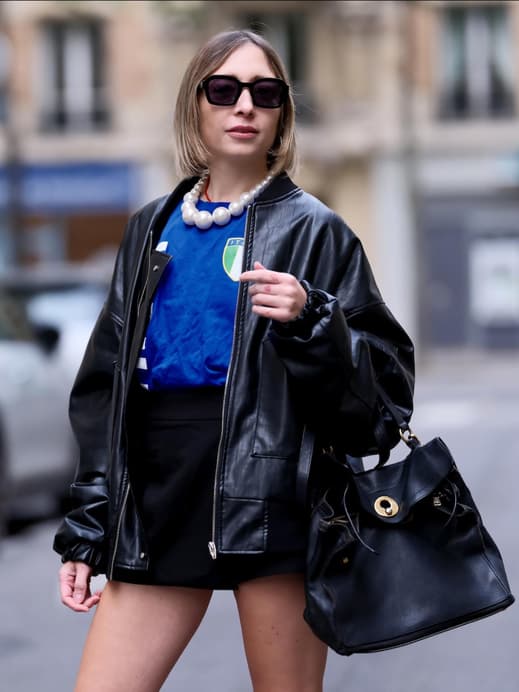 Eine Frau trägt einen schwarzen kurzen Rock, ein Italien Trikot, eine schwarze Lederjacke und eine Sonnenbrille plus Tasche.