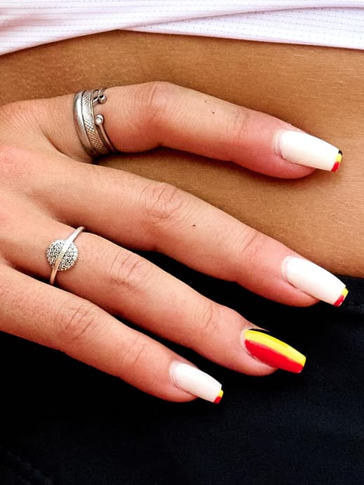 Der Bauch einer Frau mit einem Deutschlandtrikot und ihren Händen mit Ringen und Deutschlandnägeln.