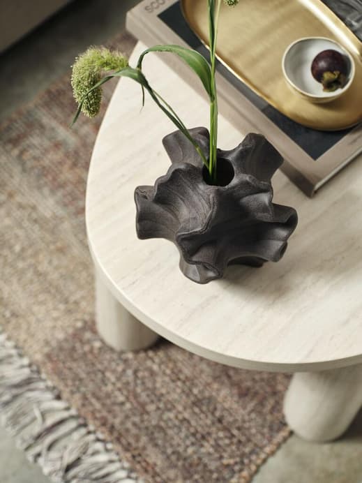 Eine organische Vase mit ein paar Gräsern auf einem Couchtisch von oben betrachtet.