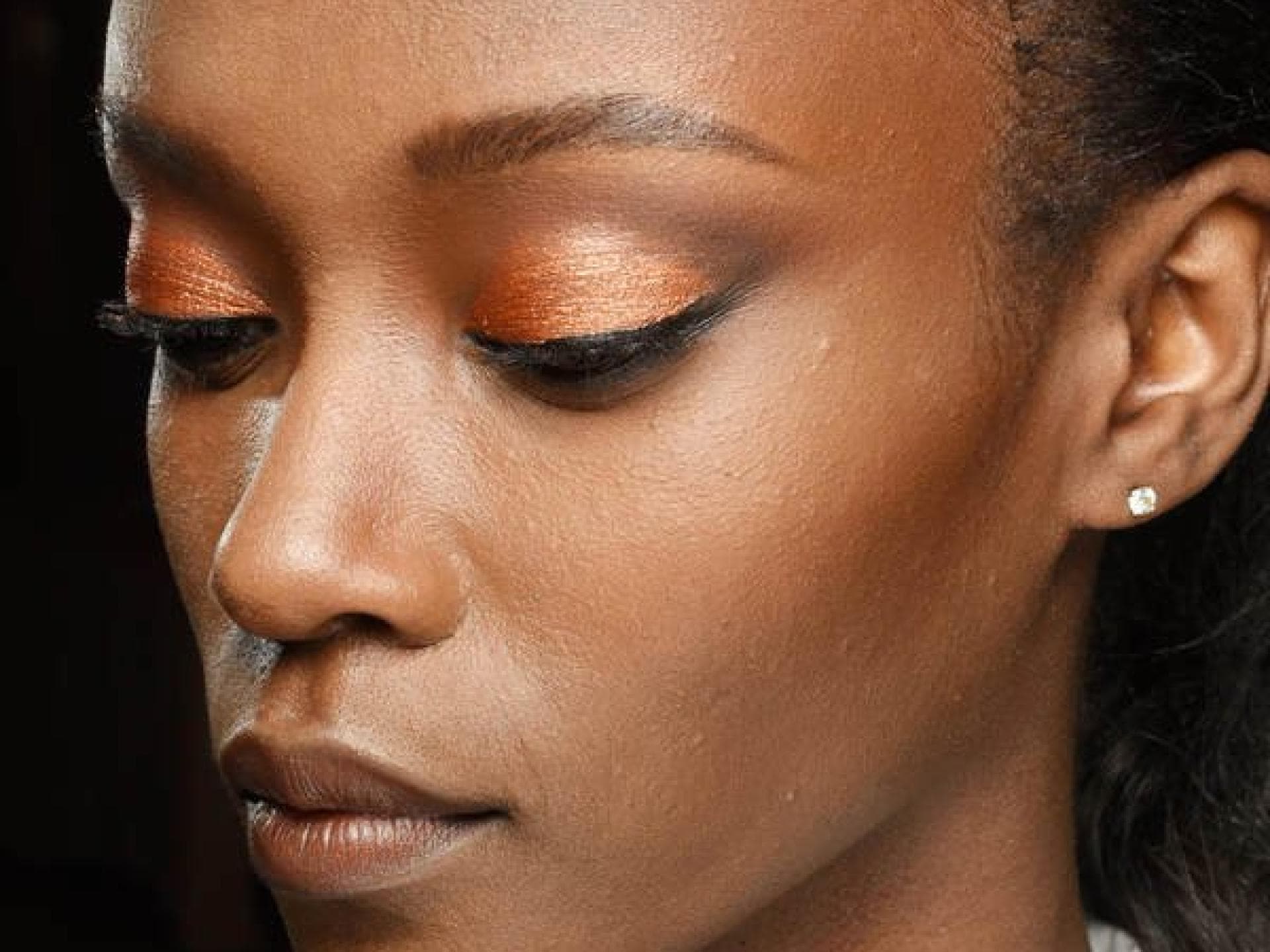 Smokey Eyes in Kupfer sind sanfter als die klassische Variante. Frau guckt nach unten und trägt Smokey Eyes in Kupfer