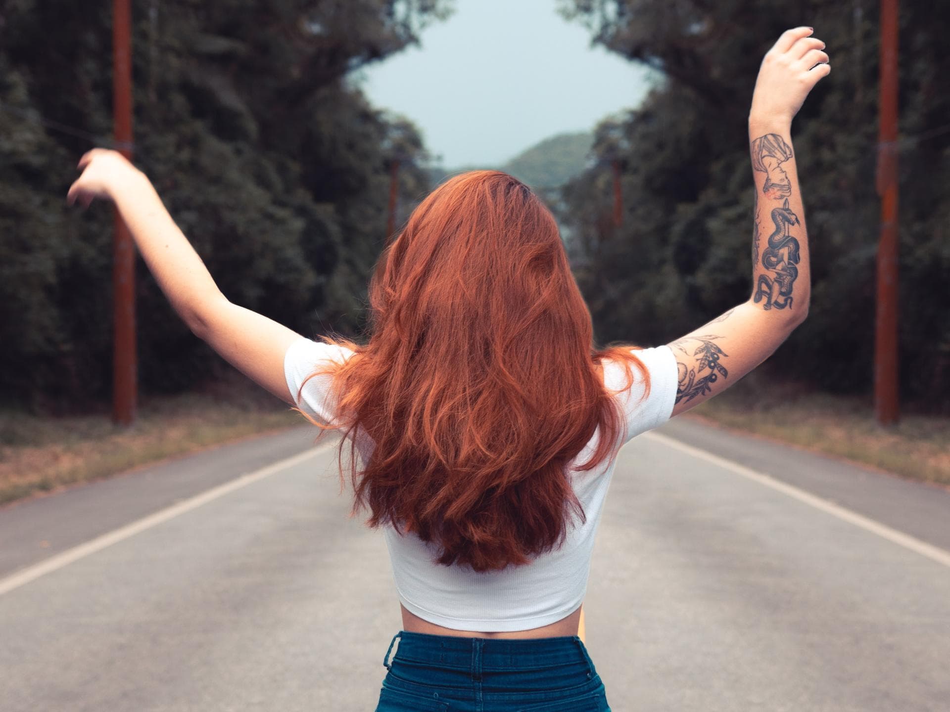 Tattoo-Trends 2020 Rothaarige Frau auf einer Straße im Wald mit Tattoos am rechten Arm