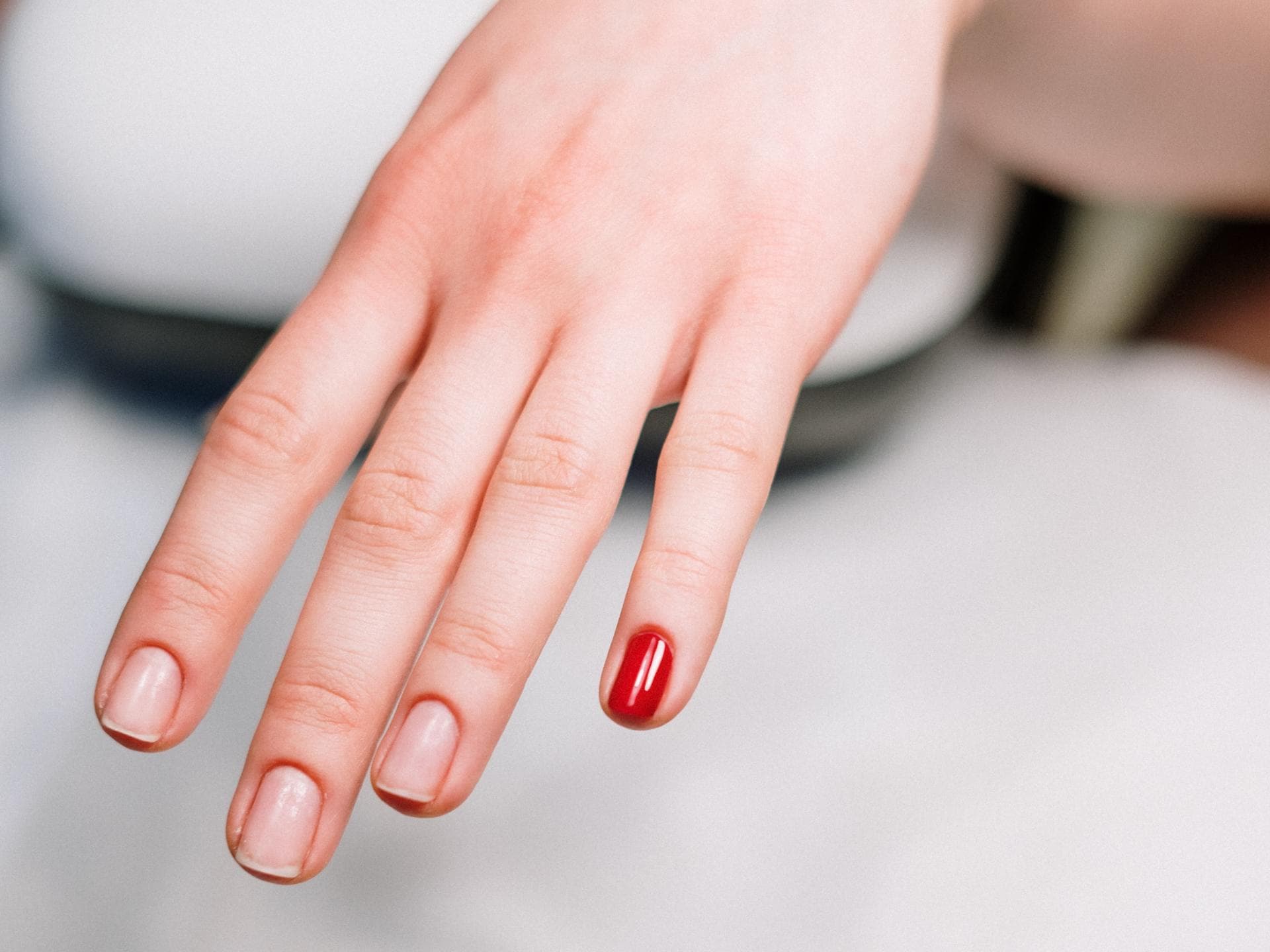 Hand mit natürlichen Nägeln und rotem Nagellack auf dem kleinen Finger