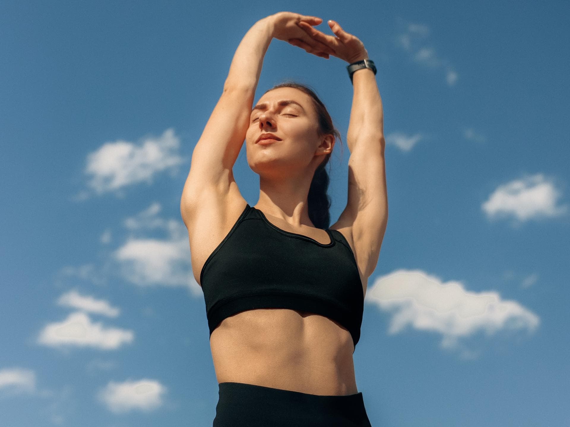 Frau mit Sport-Bh und Sporleggings streckt die Arme in den Himmel