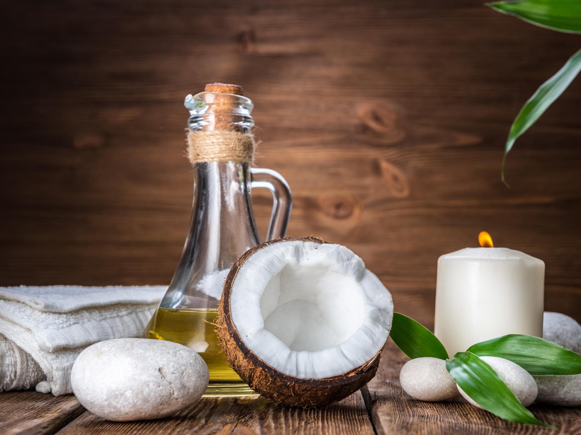Kokosöl Haare: Ölflasche steht neben einer halben Kokosnuss und einer Kerze auf einem Tisch