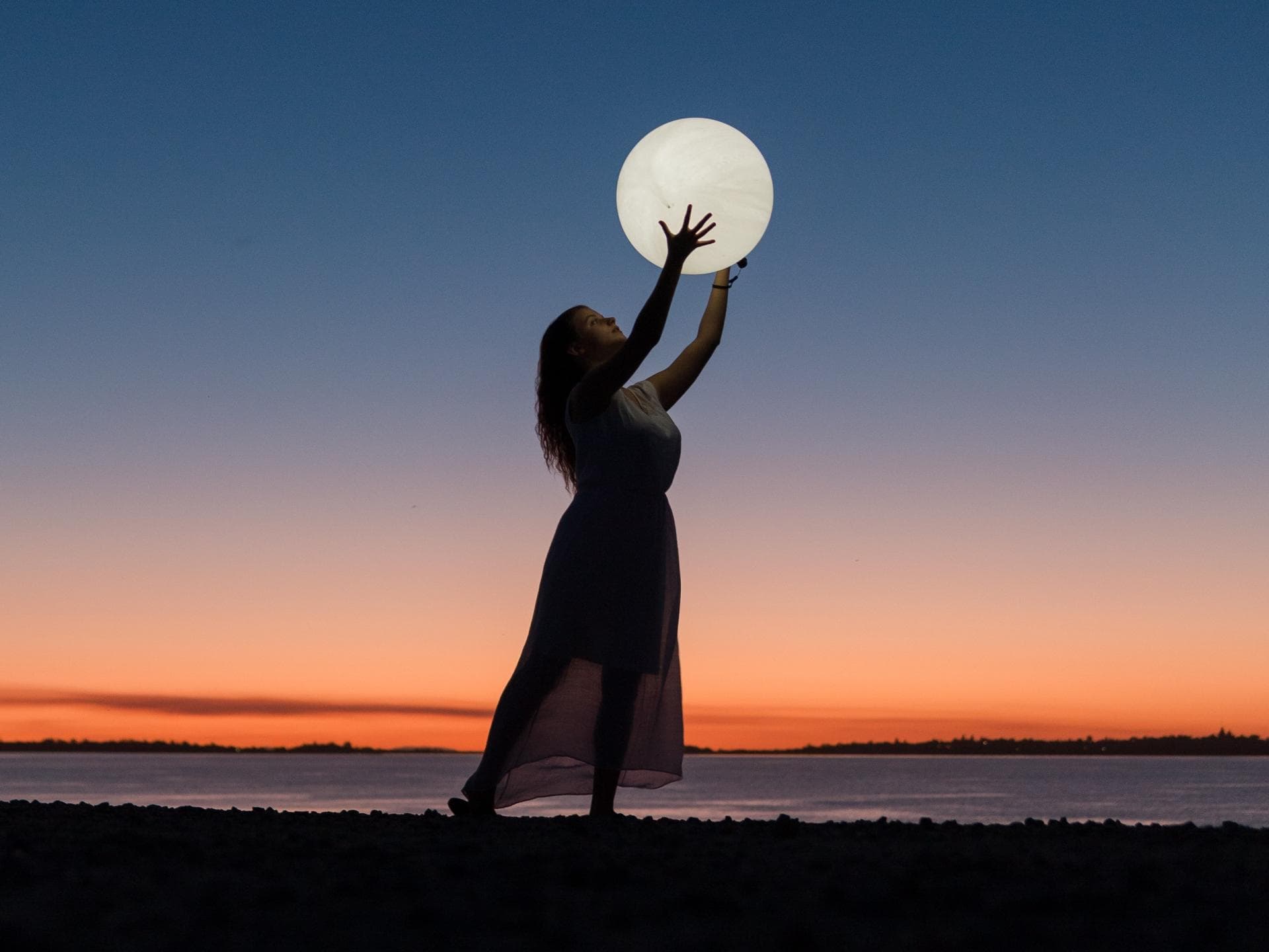 Vollmond Horoskop: Frau hält einen Vollmond in der Hand am Strand