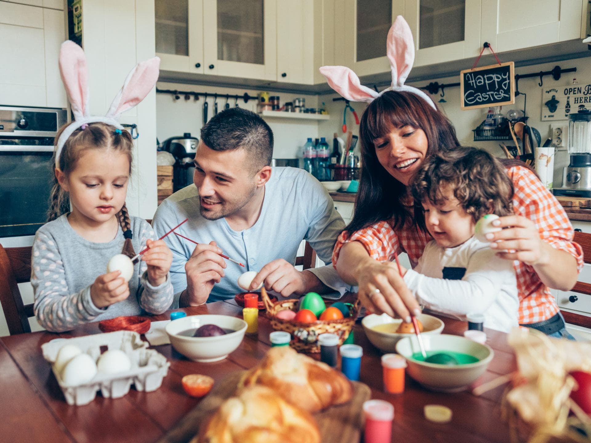 Warum feiern wir Ostern? Verständlich erklärt Warum feiern wir Ostern? Familie sitzt am Tisch und bemalt Ostereier