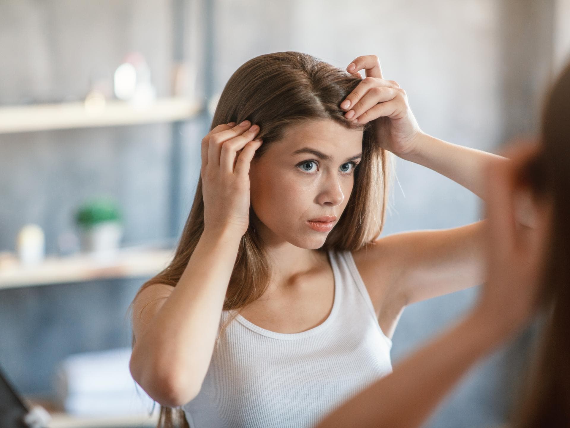 Wie schnell wachsen Haare? Frau steht vor Spiegel und schaut sich den Haaransatz an