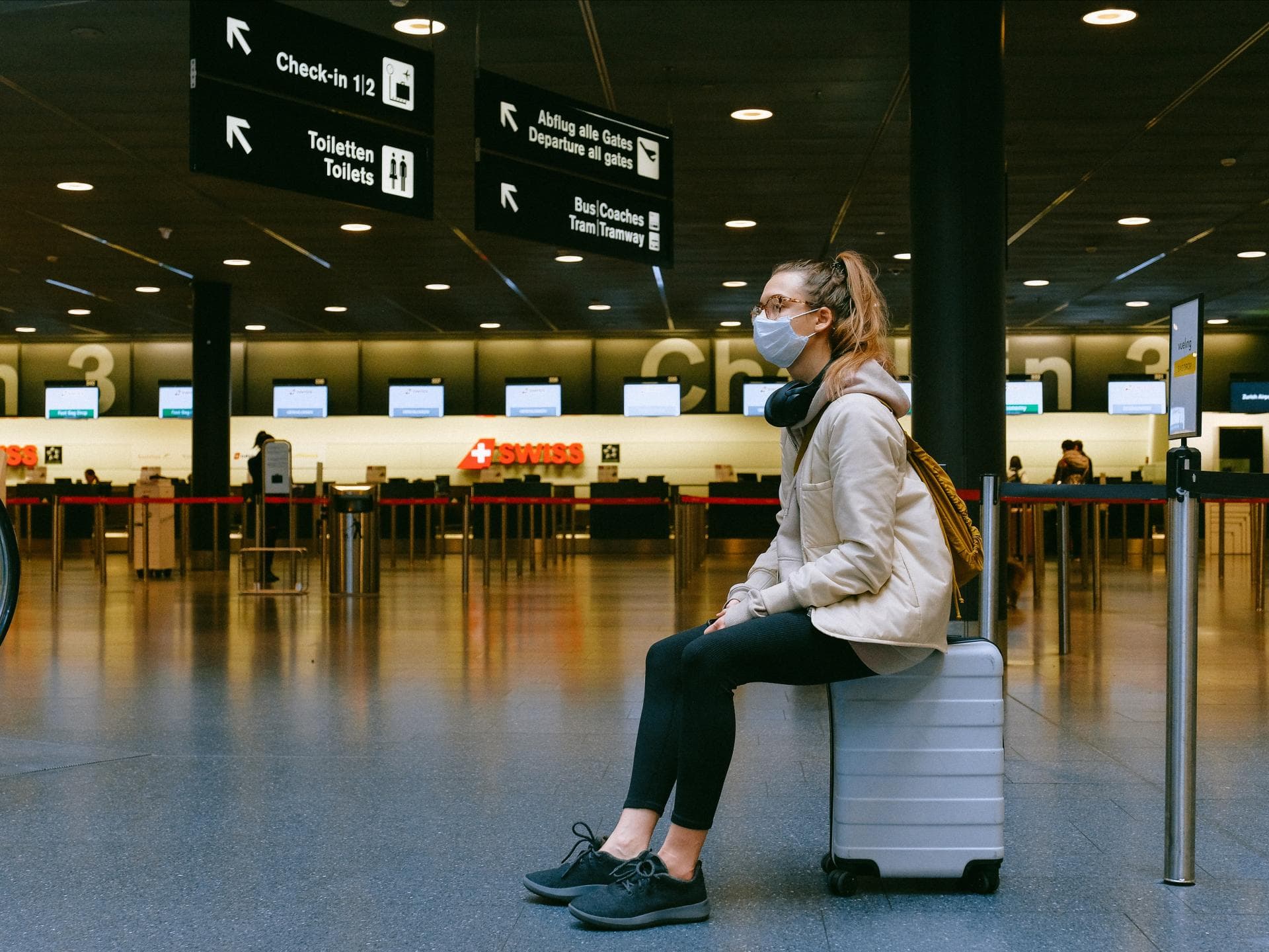 Frau sitzt am Flughafen mit Maske und Koffer