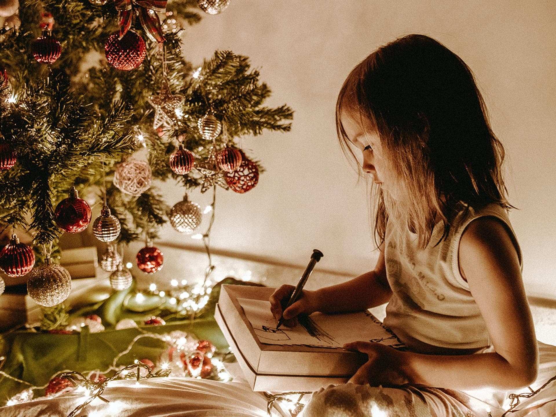 Kleines Mädchen malt vor dem Weihnachtsbaum