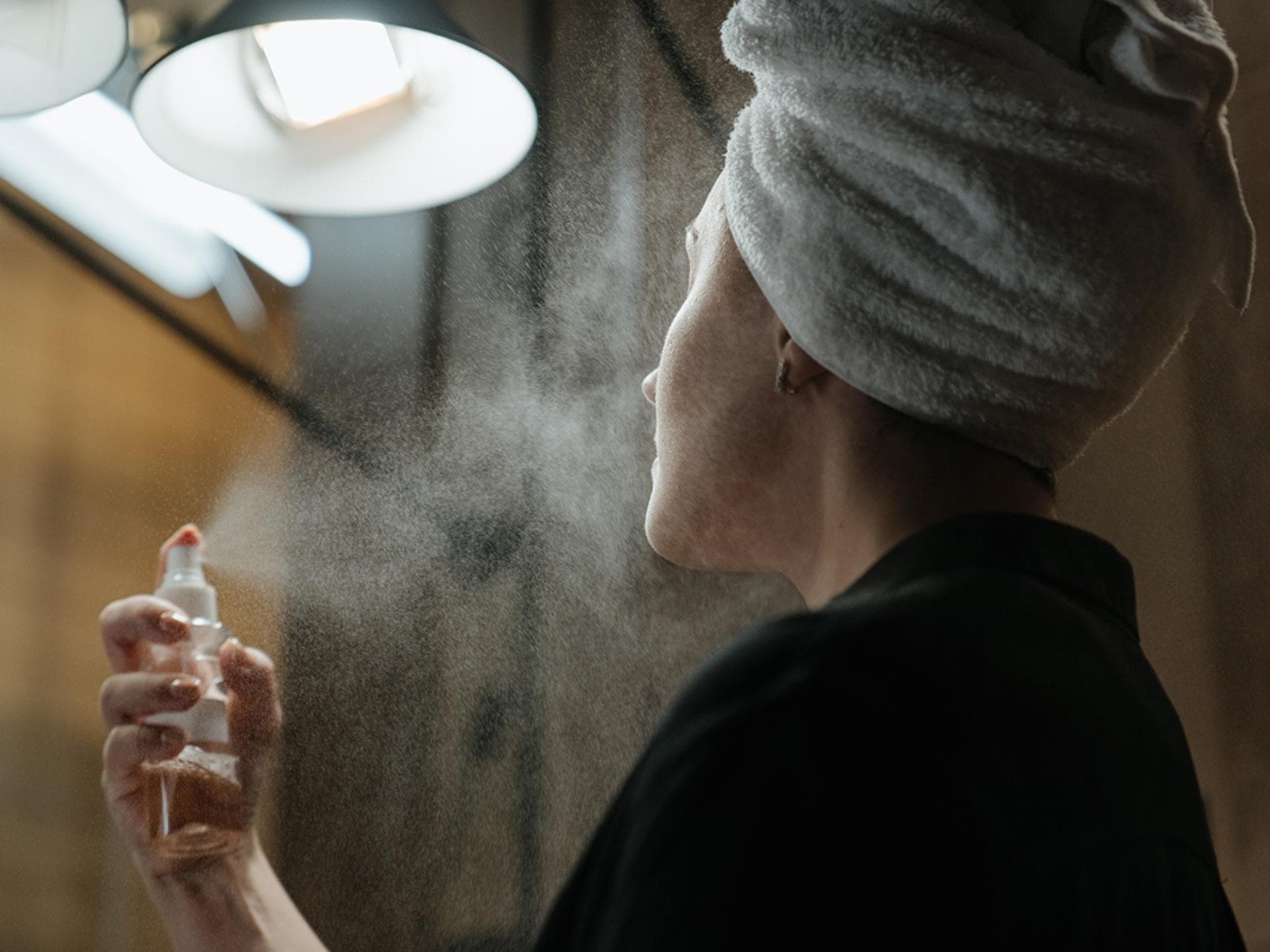 Frau sprüht Gesichtsspray auf ihr Gesicht