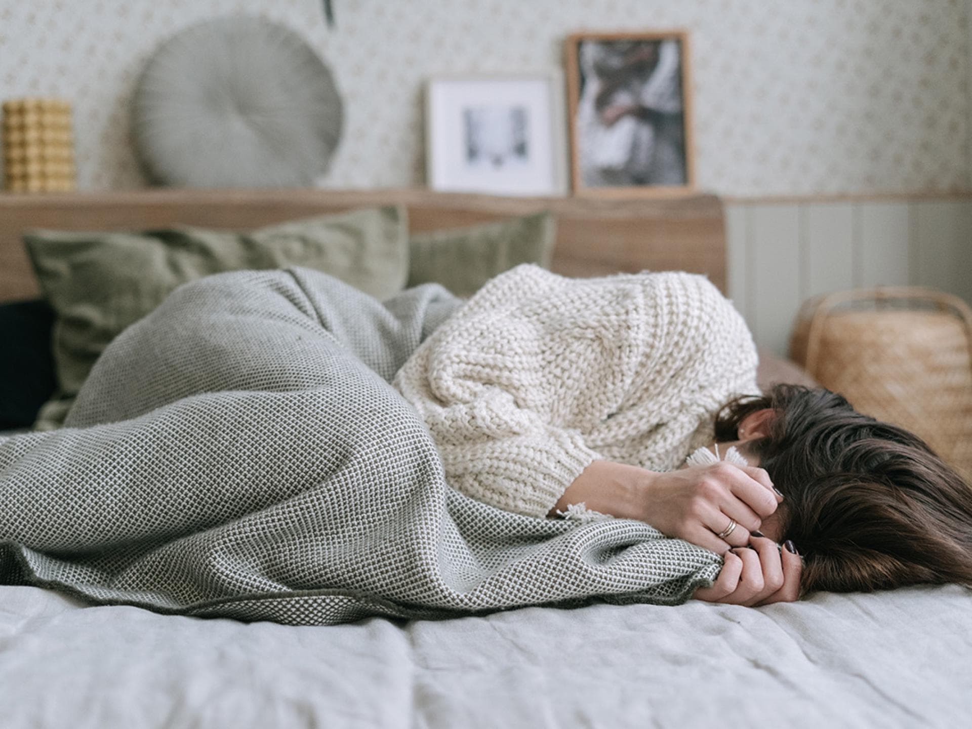 Frau im Bett mit Händen vor Gesicht 