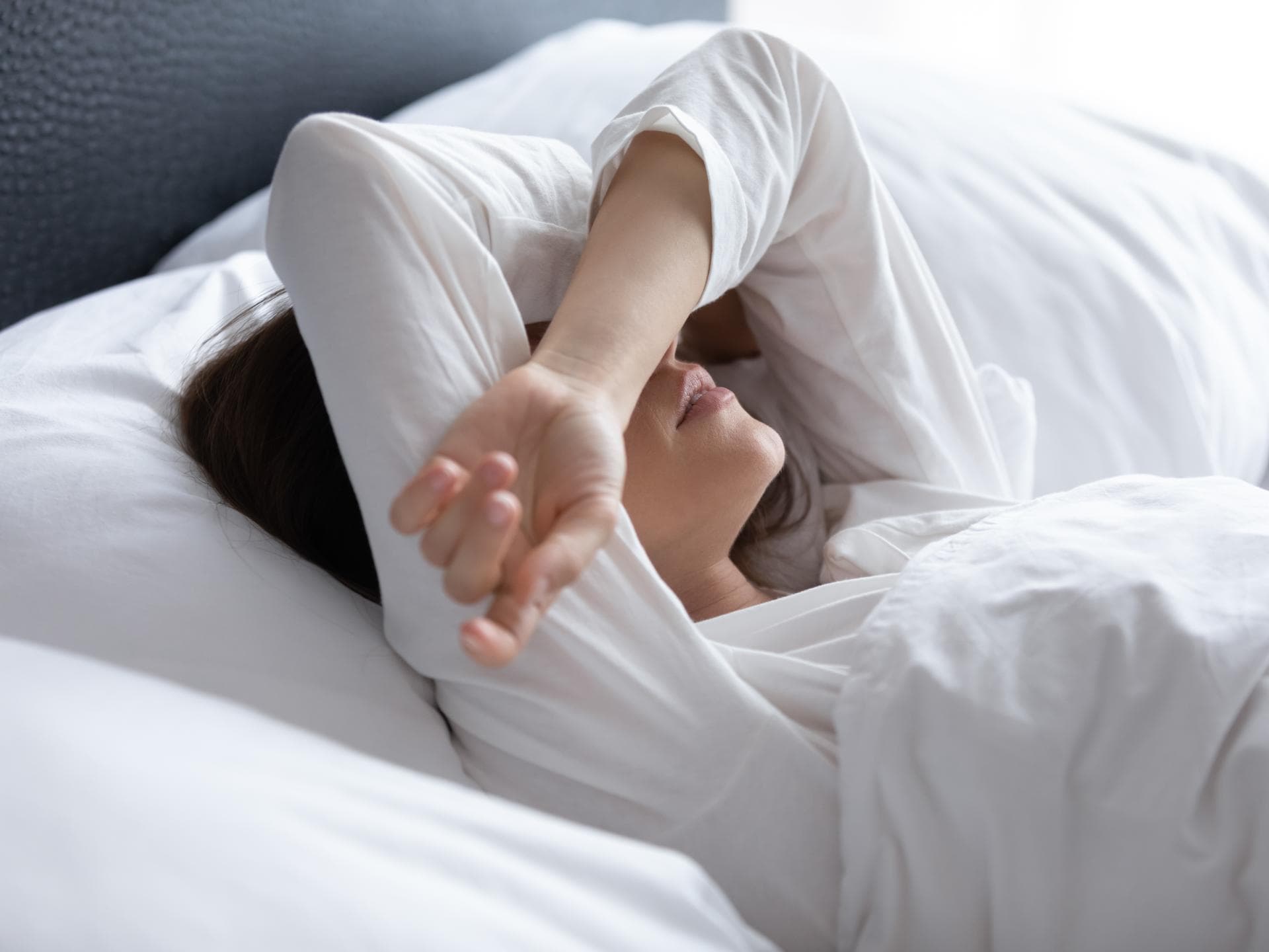 Frau rauft Arme über den Kopf zusammen und liegt im Bett