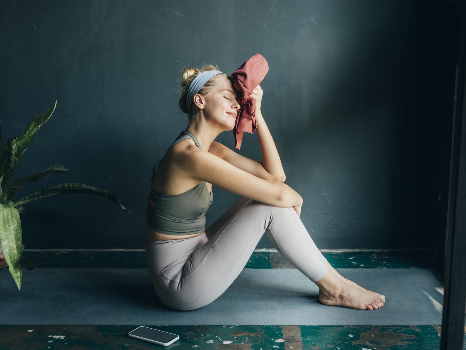 FGrau sitzt auf Yogamatte und hält sich ein Handtuch an den Kopf