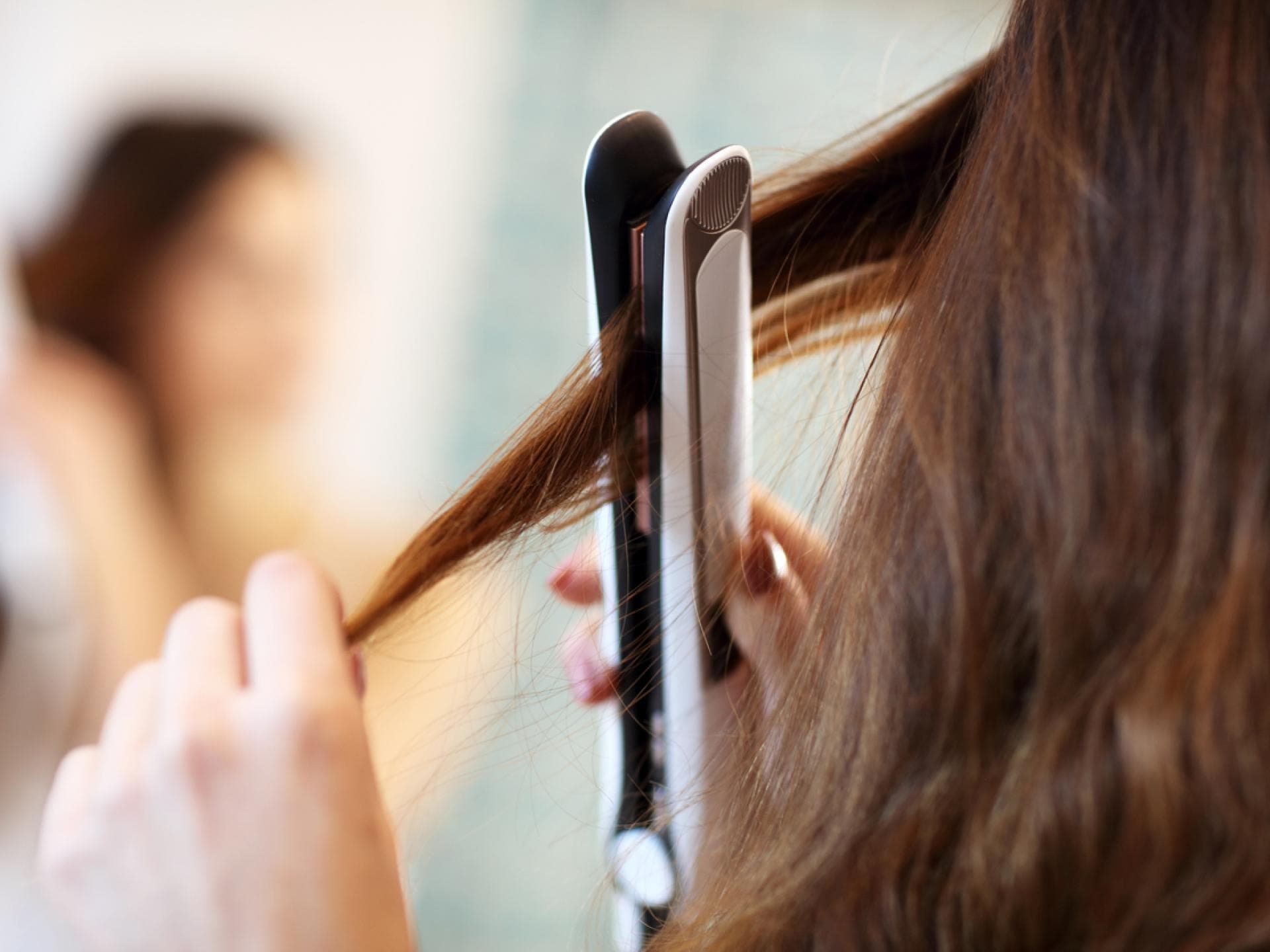 Frau glättet sich die Haare mit Dampfglätteisen