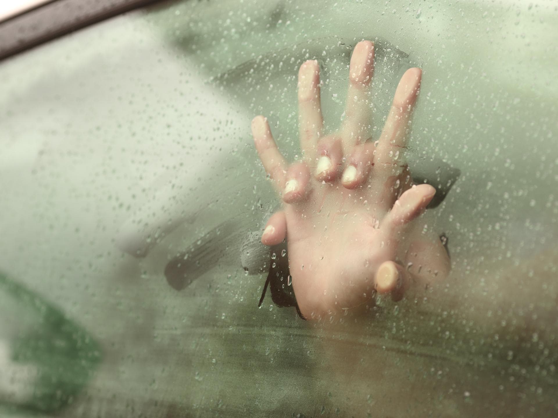 Ineinenander verschränkte Hände im Auto fassen ans Fenster