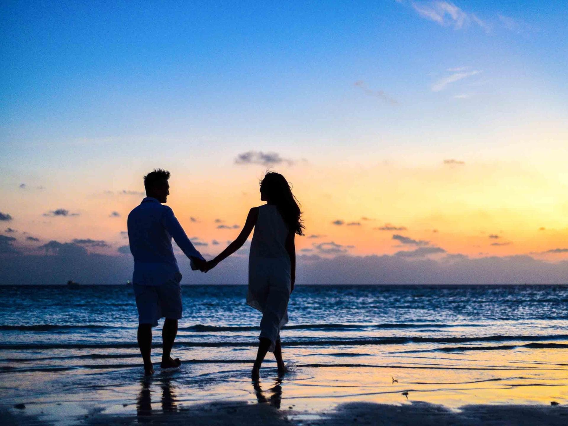 Frau und Mann halten Händchen und spazieren am Strand