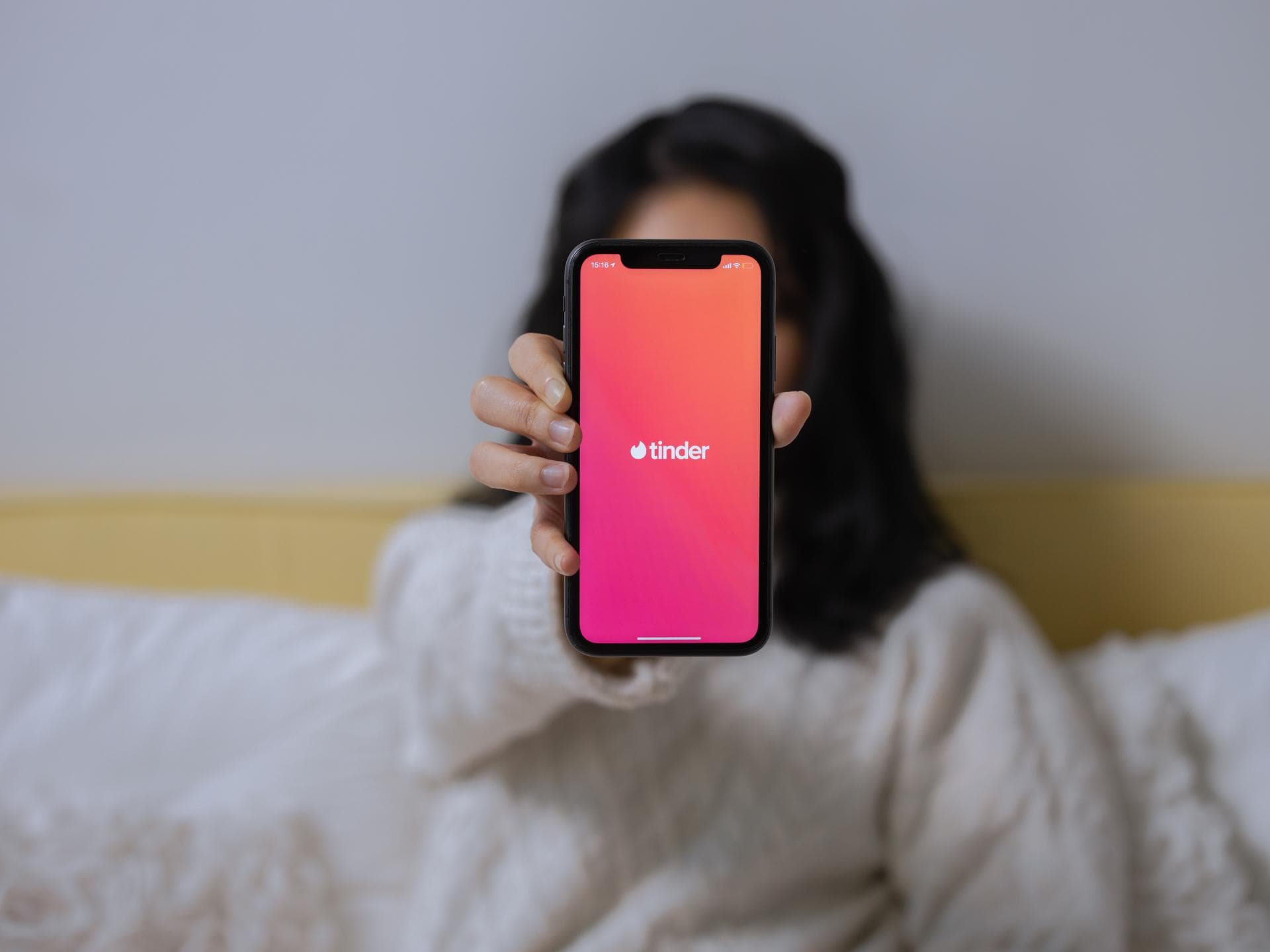 Frau hält Handy mit geöffneter Tinder-App hoch 